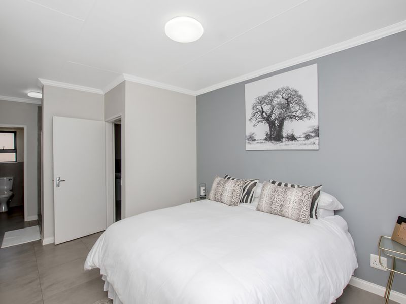 A well-maintained bedroom featuring neutral grey walls, tiled flooring, and direct access to an en-suite bathroom.