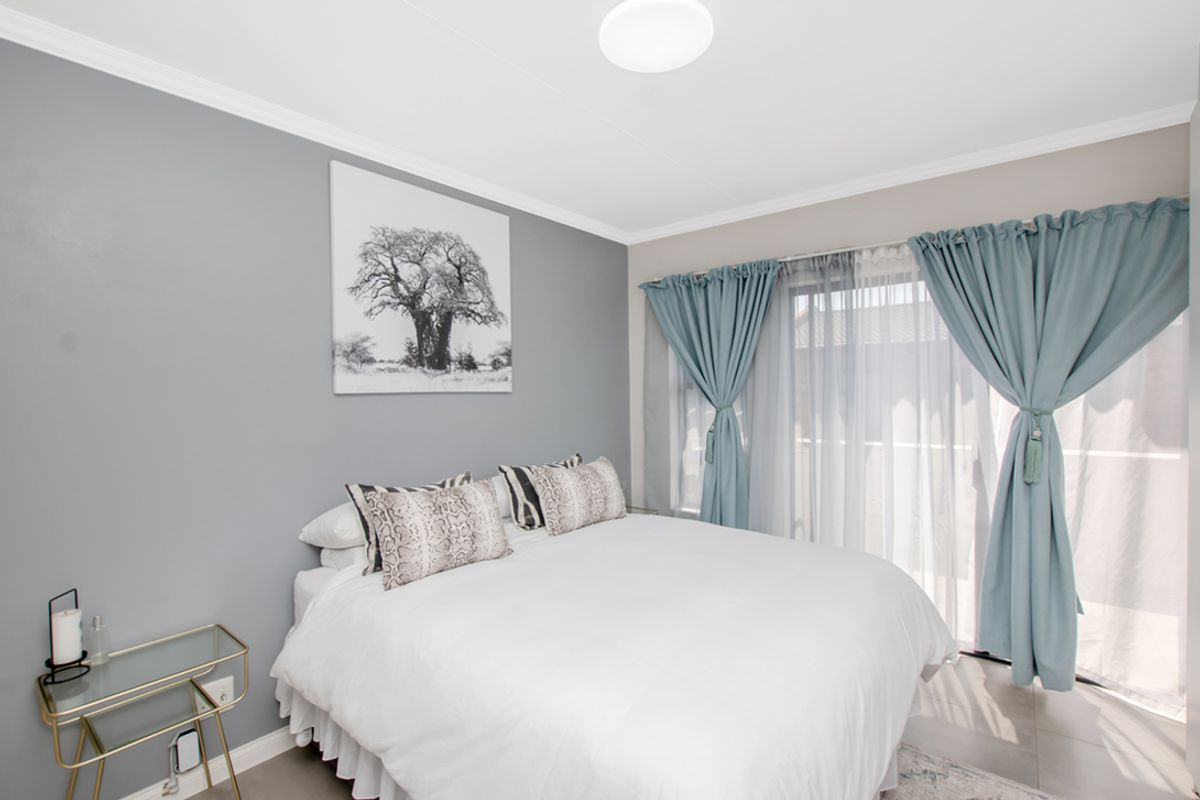 A well-maintained bedroom featuring tiled flooring, neutral grey walls, and a sliding glass door providing access to an outdoor area.