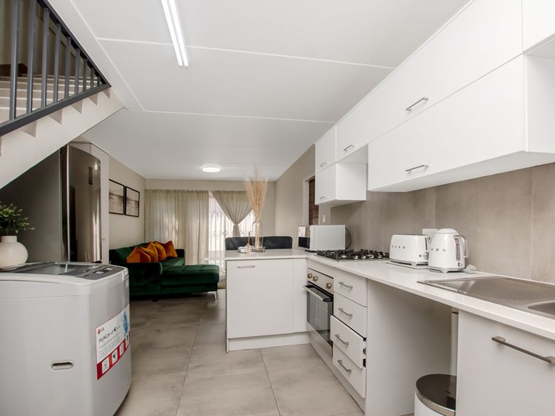 Modern open-plan kitchen and living area featuring sleek white cabinetry, gas hob, built-in oven, and tiled flooring, with an adjacent staircase.