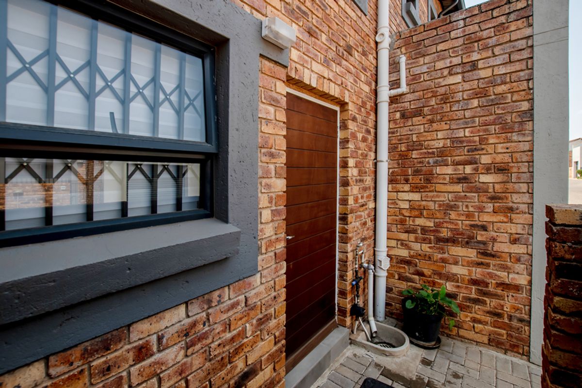 A side exterior view of the townhouse featuring face brick walls, a secure entrance door, and functional external plumbing fixtures.