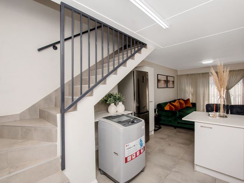 Open-plan living area featuring a modern tiled staircase with metal balustrade, integrated kitchen cabinetry, and a central island, creating a functional and cohesive space.