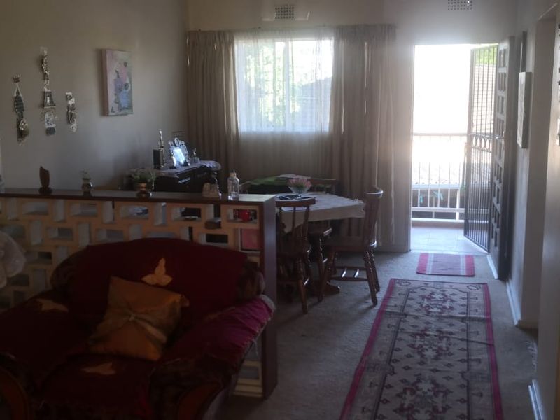 Open plan living and dining area featuring a decorative breeze block partition, carpeted flooring, and direct access to an outdoor balcony through a security gate.