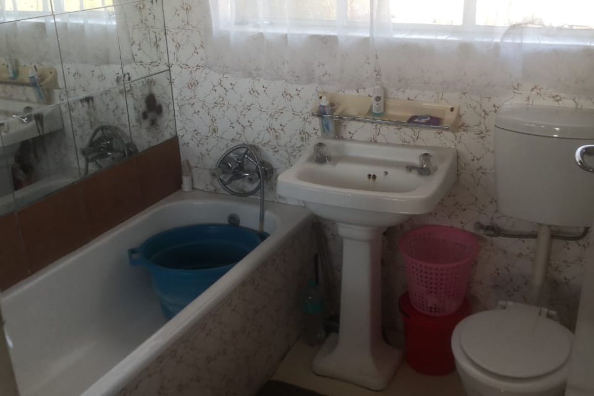 A dated bathroom featuring a pedestal basin, bathtub, and toilet with original wall tiling, offering potential for a modern renovation.