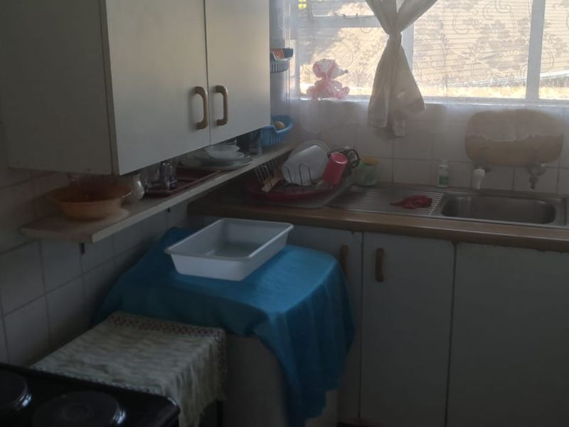 A dated kitchen featuring original cabinetry, a stainless steel sink, and tiled backsplash, offering potential for a modern renovation.