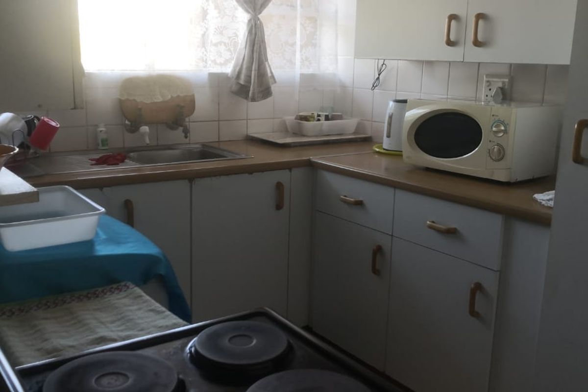 A compact, dated kitchen featuring laminate countertops, built-in cabinetry, a stainless steel sink, and an electric stove with a tiled backsplash.