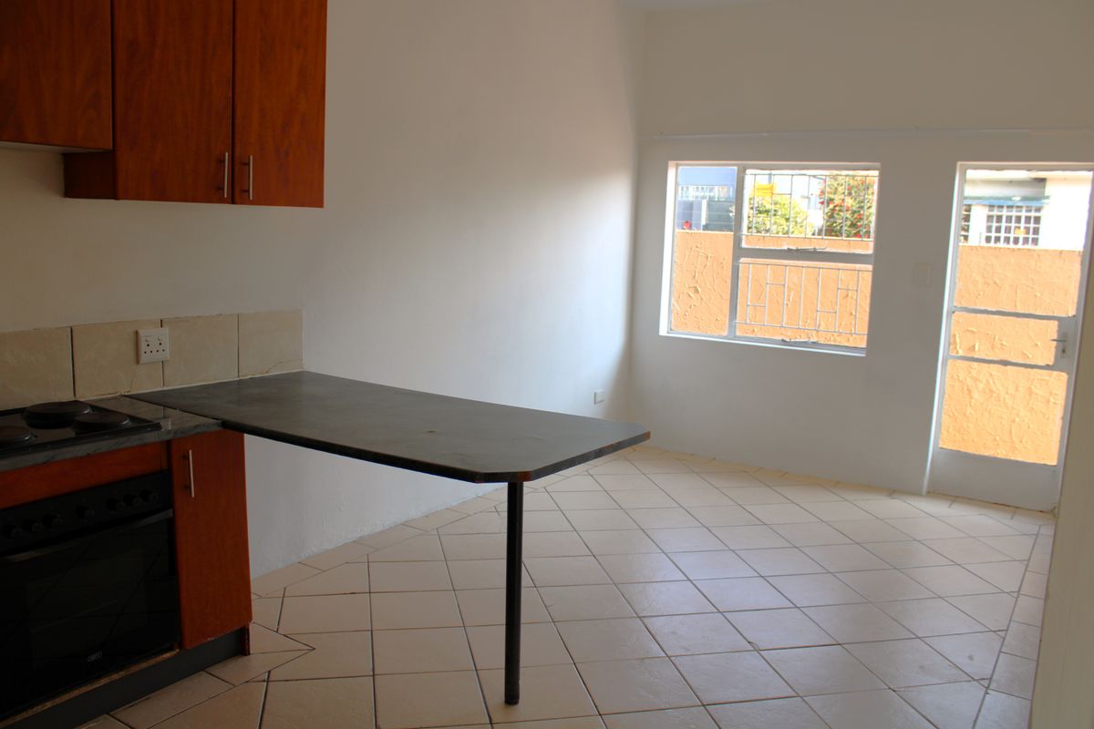 An empty kitchen featuring wooden cabinetry, a built-in oven and hob, a breakfast counter, and tiled flooring with direct access to an outdoor area.