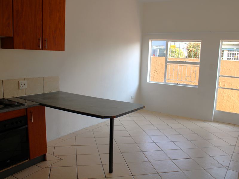 An empty kitchen featuring wooden cabinetry, a built-in oven and hob, a breakfast counter, and tiled flooring with direct access to an outdoor area.