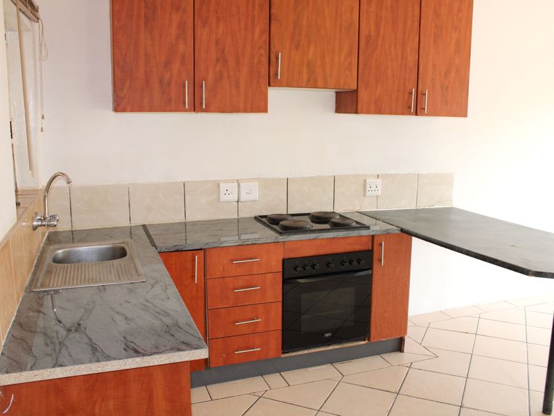 A functional kitchen featuring wood-look cabinetry, stone-effect countertops, a built-in oven with hob, and tiled flooring.