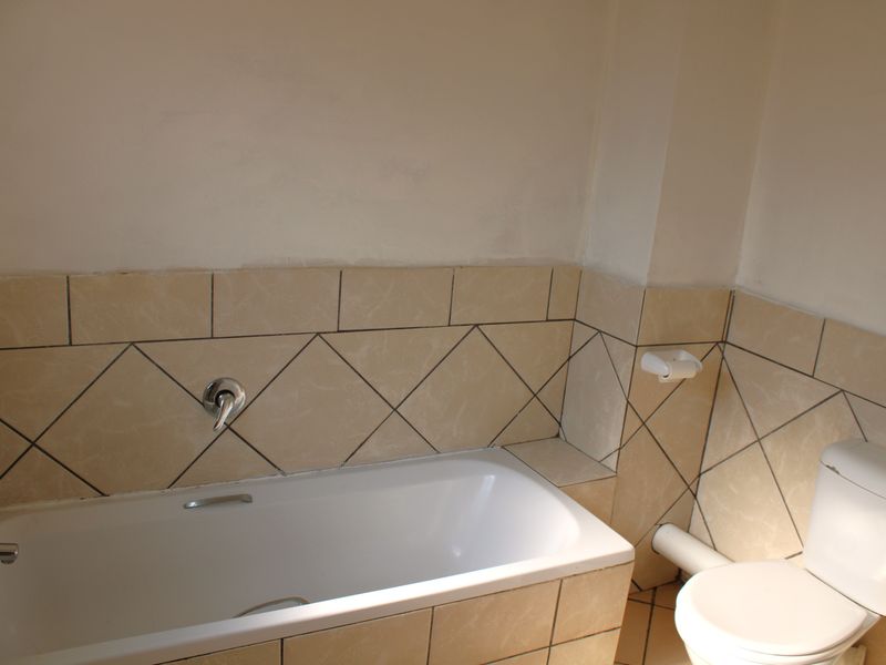A functional bathroom featuring a bathtub and toilet with neutral tiled splashbacks, currently requiring minor finishing touches to the wall paint.