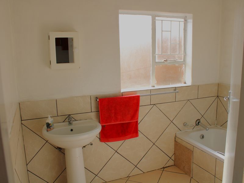 A functional bathroom featuring a pedestal basin, bathtub with tiled surround, and a window with security bars.