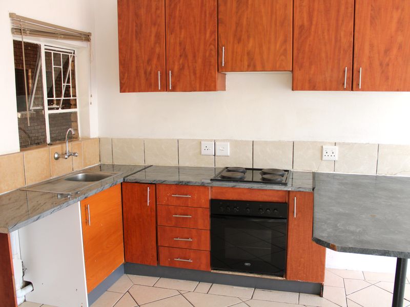 A functional kitchen featuring wood-look cabinetry, granite-style countertops, a built-in oven with electric hob, and tiled flooring.