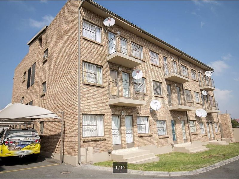 A multi-story apartment building featuring a face brick exterior, private balconies with metal railings, and an adjacent covered carport area.