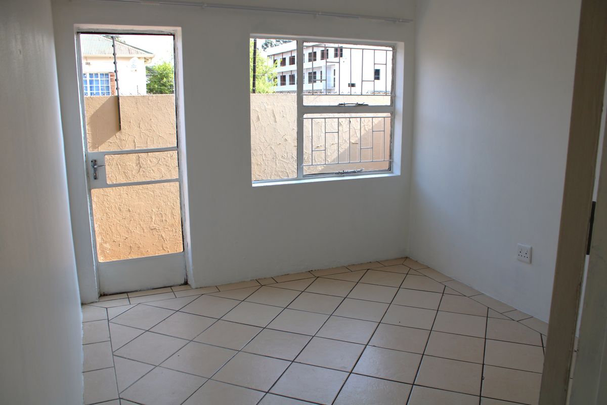 An empty bedroom featuring tiled flooring, a security gate, and window security bars, providing a blank canvas for personalization.