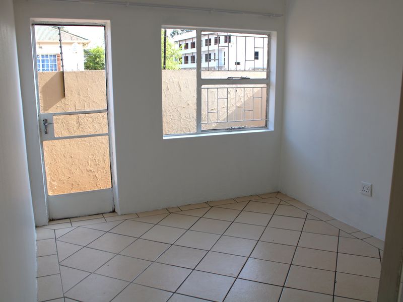 An empty bedroom featuring tiled flooring, a security gate, and window security bars, providing a blank canvas for personalization.