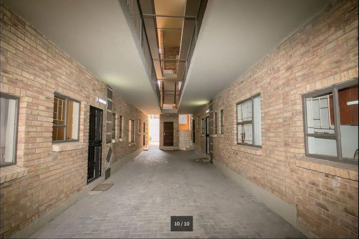 A covered outdoor hallway or walkway featuring exposed brick walls, paved flooring, and access to multiple apartment units.