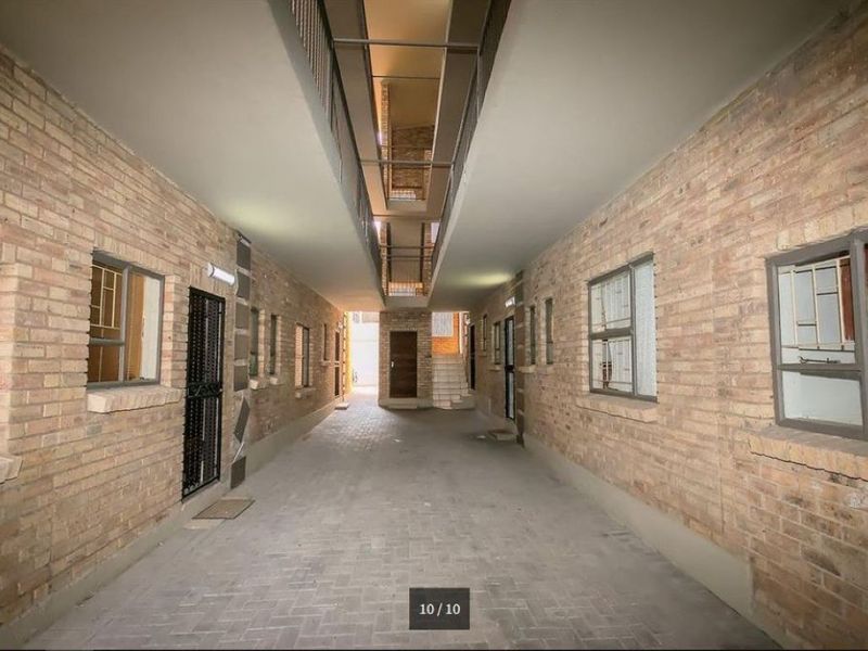 A covered outdoor hallway or walkway featuring exposed brick walls, paved flooring, and access to multiple apartment units.