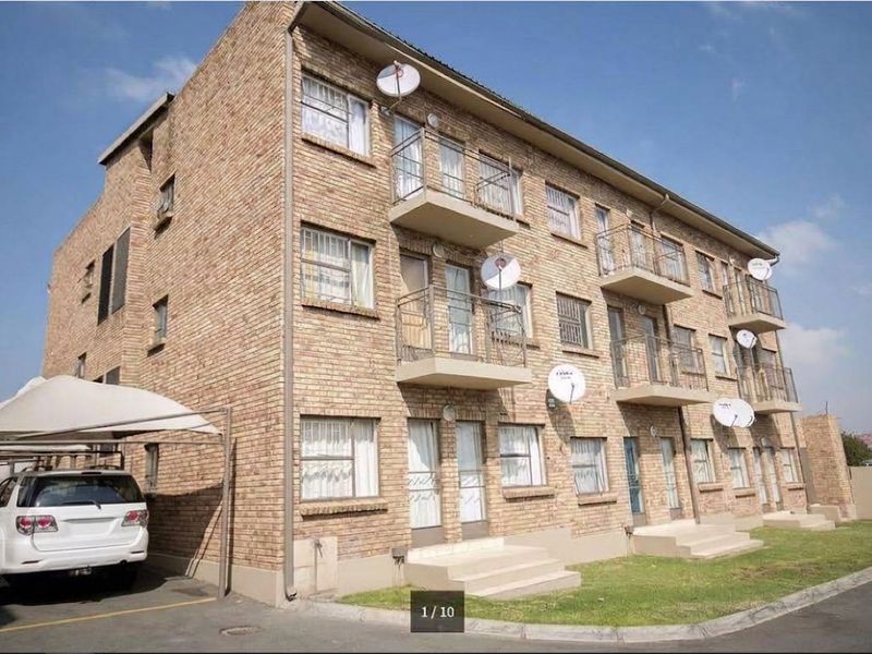 Exterior view of a multi-story face brick apartment building featuring private balconies, ground-level access, and a covered carport parking area.