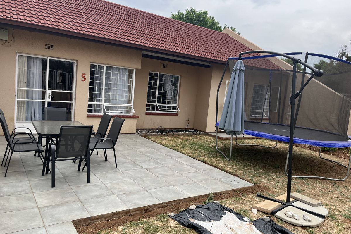 Rear view of the townhouse featuring a tiled patio area, sliding glass doors, security bars on windows, and a private garden space.