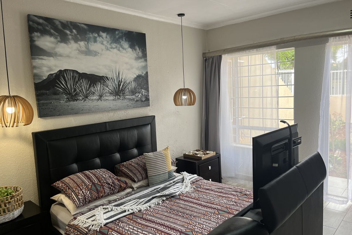 A well-maintained bedroom featuring tiled flooring, a large window with security bars, and modern pendant lighting.