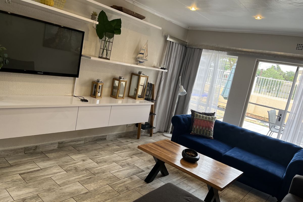 A bright living room featuring wood-look tiled flooring, recessed ceiling lighting, and large sliding glass doors providing access to the outdoor patio area.