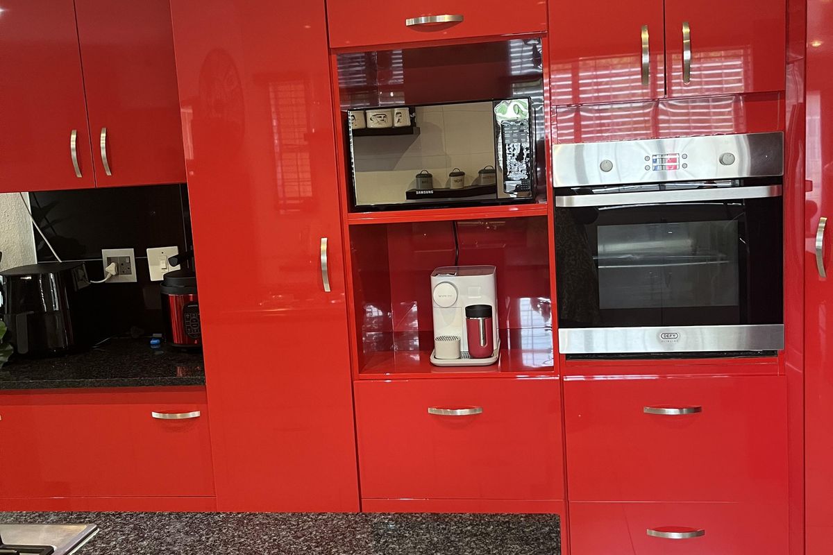 Modern kitchen featuring high-gloss red cabinetry, granite countertops, and integrated stainless steel oven and microwave.