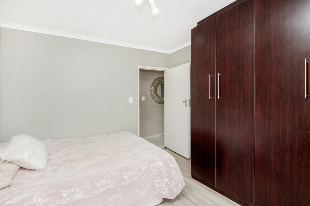 A bedroom featuring built-in dark wood cabinetry and light-toned flooring, with an adjacent doorway leading to another room.