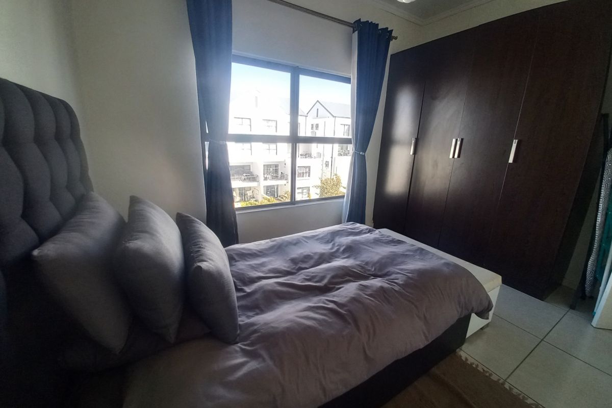 A bedroom featuring built-in dark wood cabinetry and tiled flooring, offering natural light through a window with views of the surrounding apartment complex.