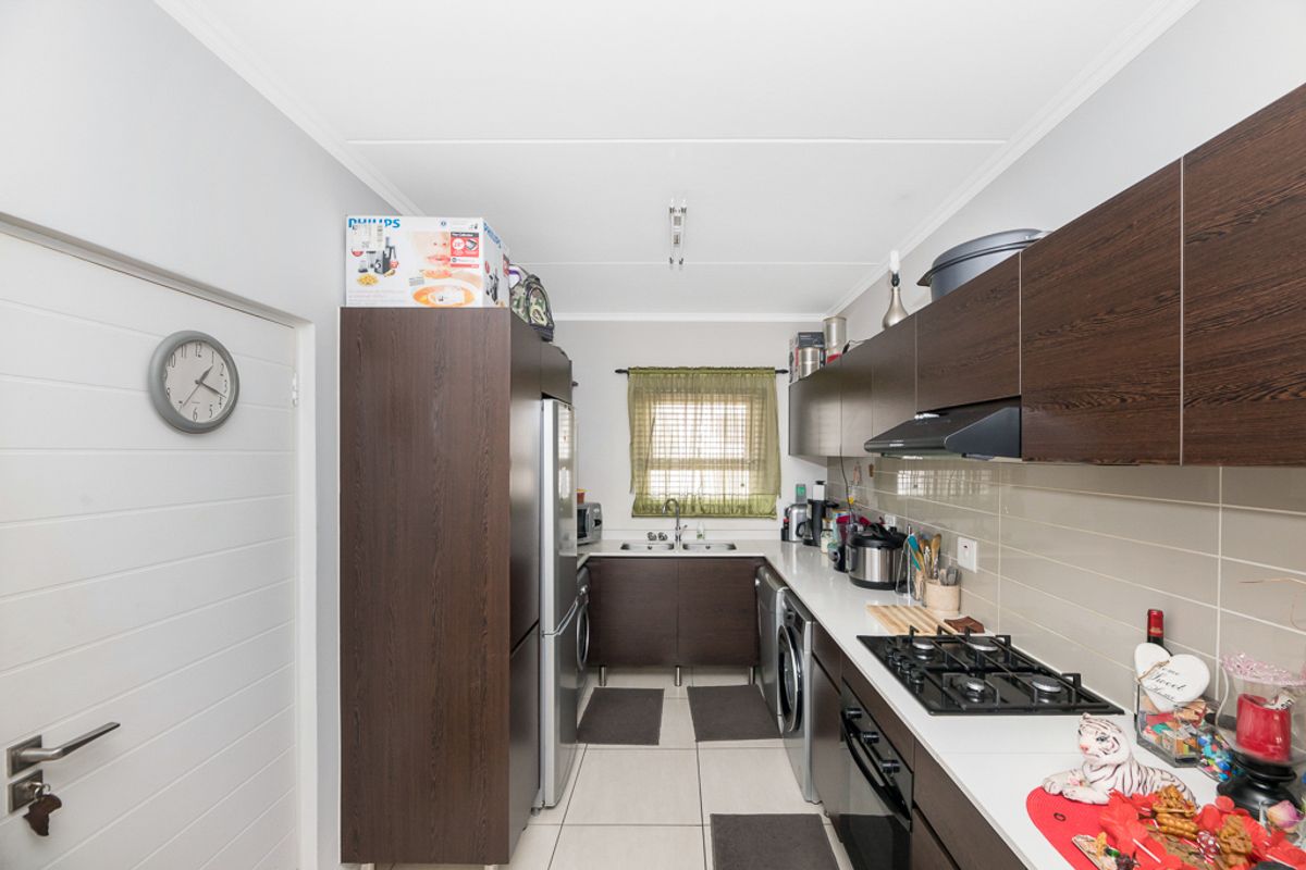 A functional galley-style kitchen featuring dark wood cabinetry, a built-in gas hob, extractor fan, and tiled flooring with integrated appliance spaces.