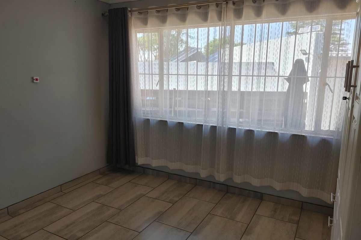 A bright, empty bedroom featuring neutral tiled flooring, large windows with security bars, and neutral wall finishes.