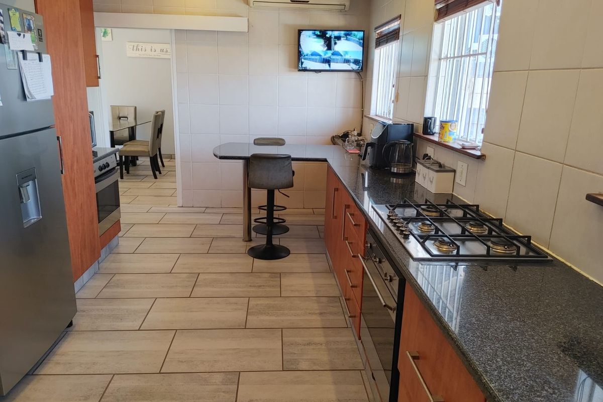 A functional kitchen featuring granite countertops, a built-in gas hob, oven, and tiled flooring, with an integrated breakfast bar area.