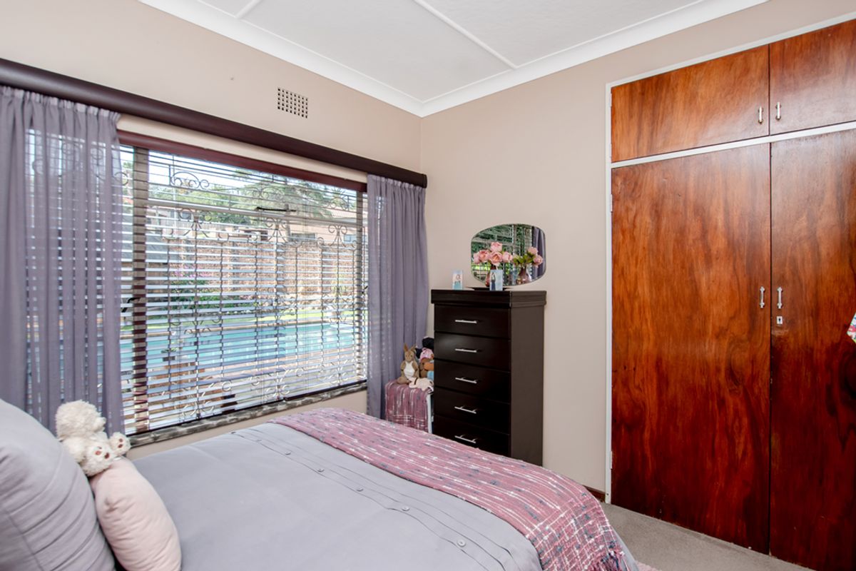 A bedroom featuring built-in wooden cupboards and a window with security bars overlooking the pool area.