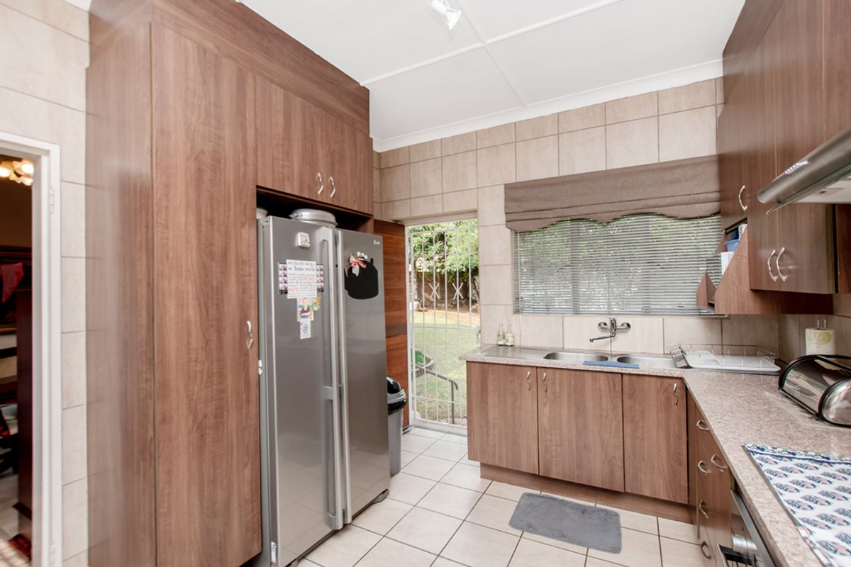 A functional kitchen featuring wood-look cabinetry, tiled splashbacks, a double sink, and direct access to the rear garden area.