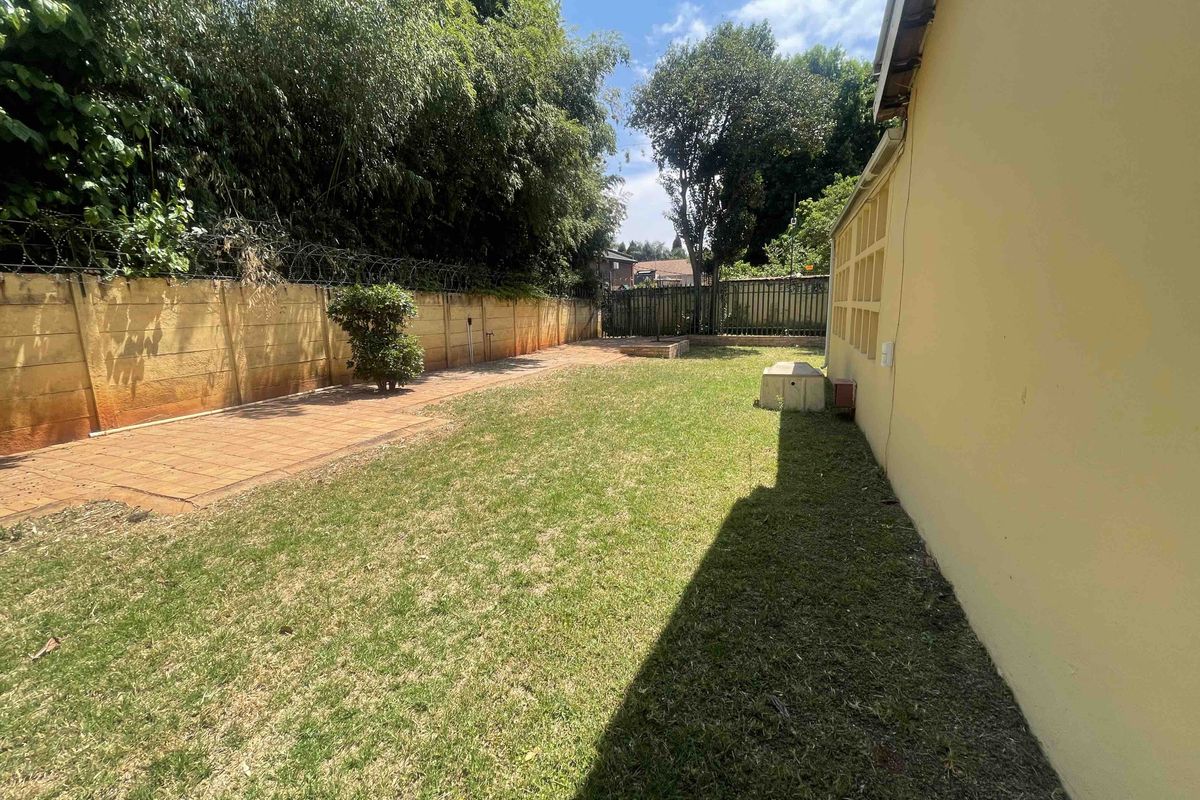 A private rear garden featuring a lawn area, paved section, and perimeter boundary walls with security fencing.