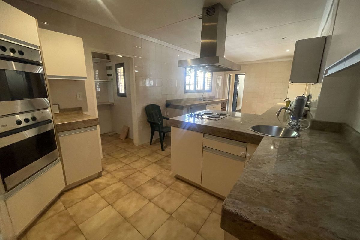Spacious kitchen featuring built-in double ovens, a central island with a hob and extractor fan, stone countertops, and an adjacent scullery area.
