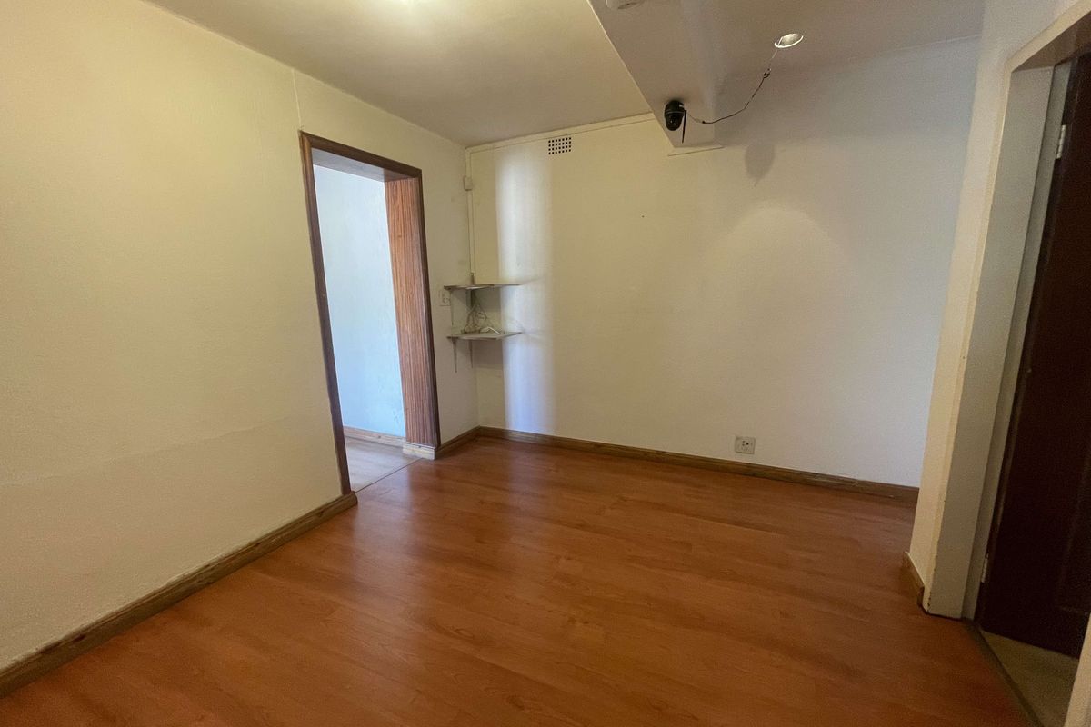 An empty room featuring laminate wood flooring, neutral walls, and a doorway leading to an adjacent space.
