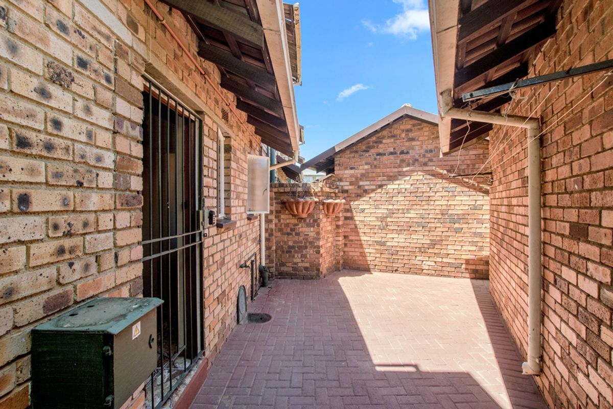 A private, paved courtyard area enclosed by face-brick walls, featuring a secure metal gate and exposed structural brickwork.