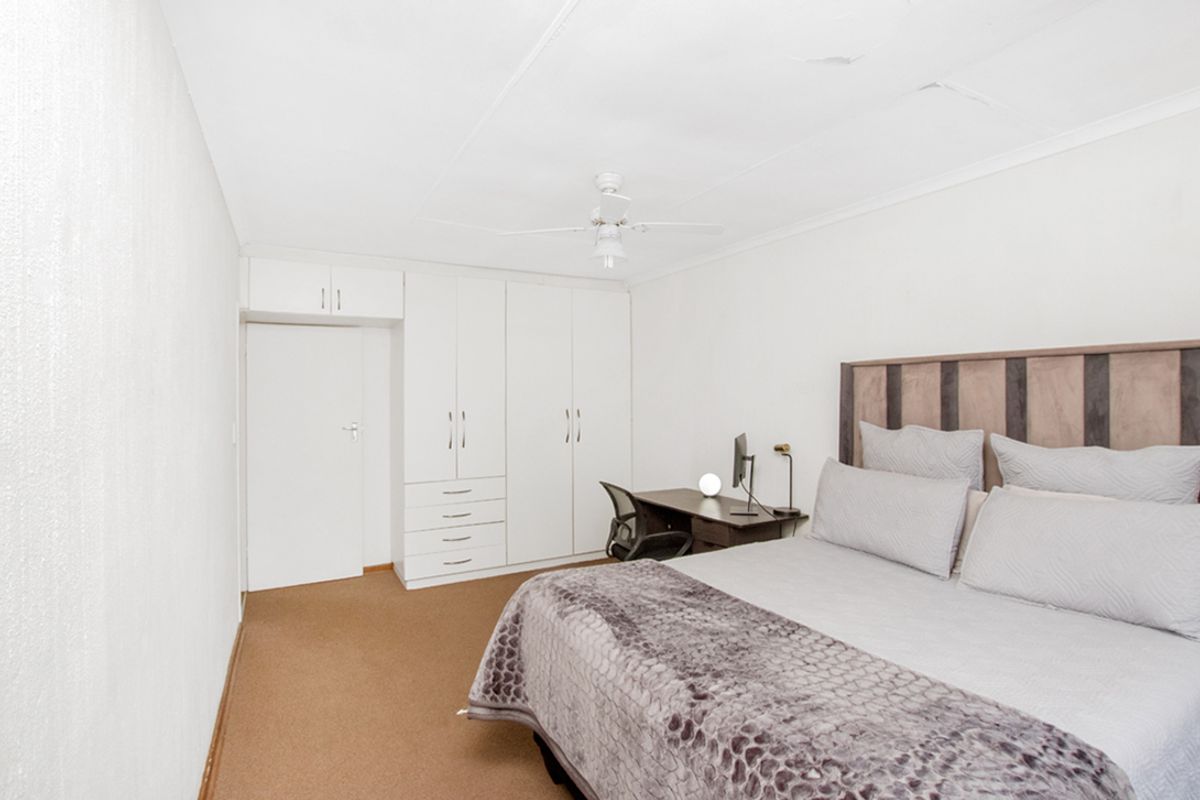 A bedroom featuring built-in white cabinetry, a ceiling fan, and neutral carpeting. The space offers functional storage and a clean, simple layout.