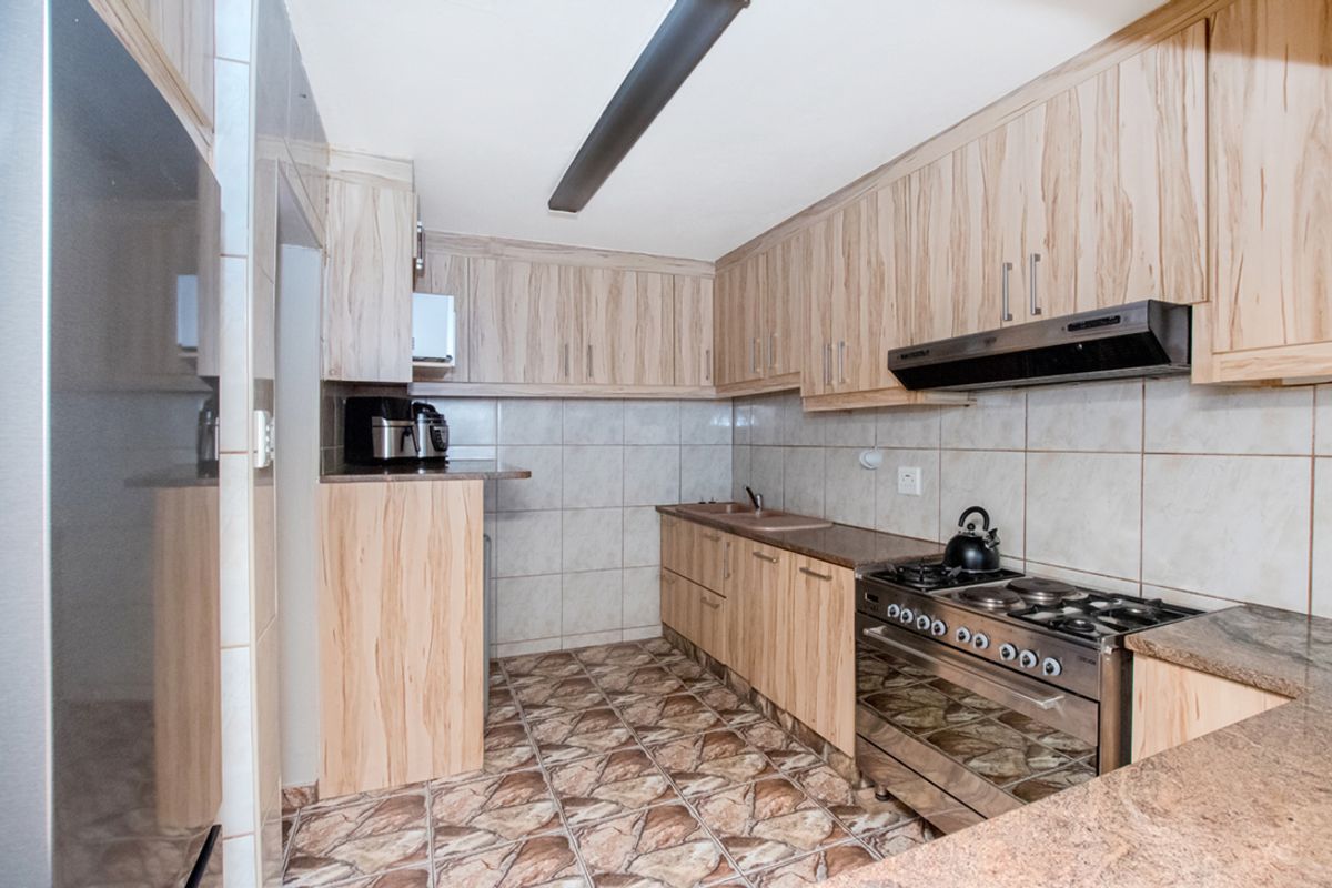 A functional kitchen featuring wood-look cabinetry, granite countertops, tiled splashbacks, and a built-in gas stove with an extractor fan.