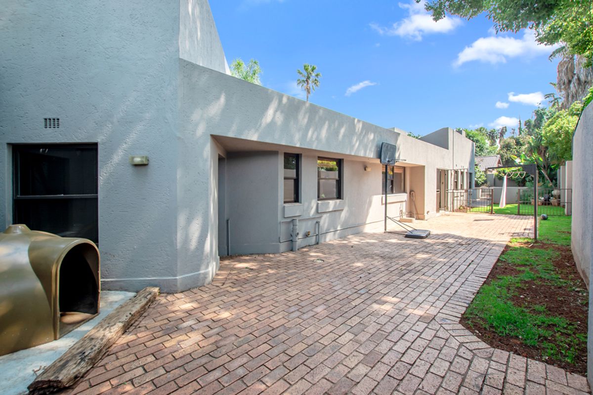 A spacious rear exterior area featuring paved patio space, established garden borders, and direct access to the main dwelling structure.