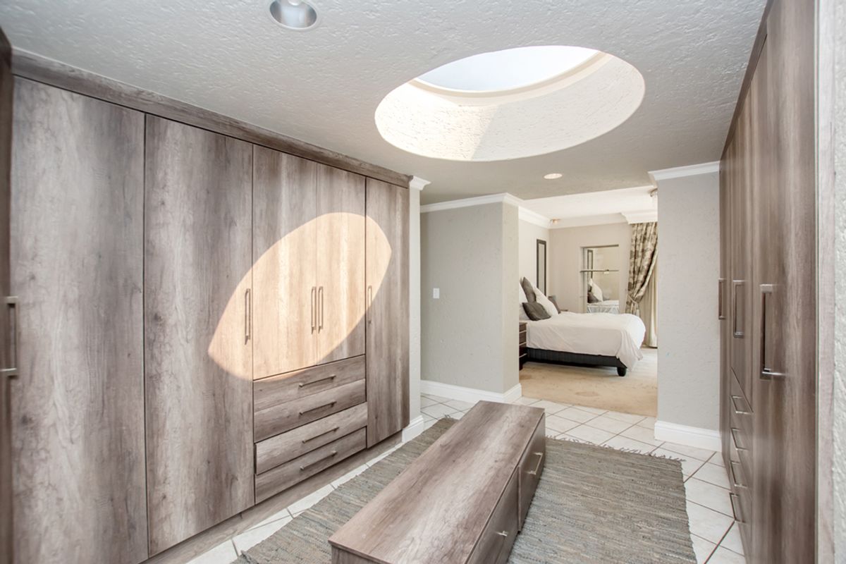 A spacious walk-in dressing room featuring extensive built-in cabinetry, tiled flooring, and a circular skylight, leading into a connected bedroom area.