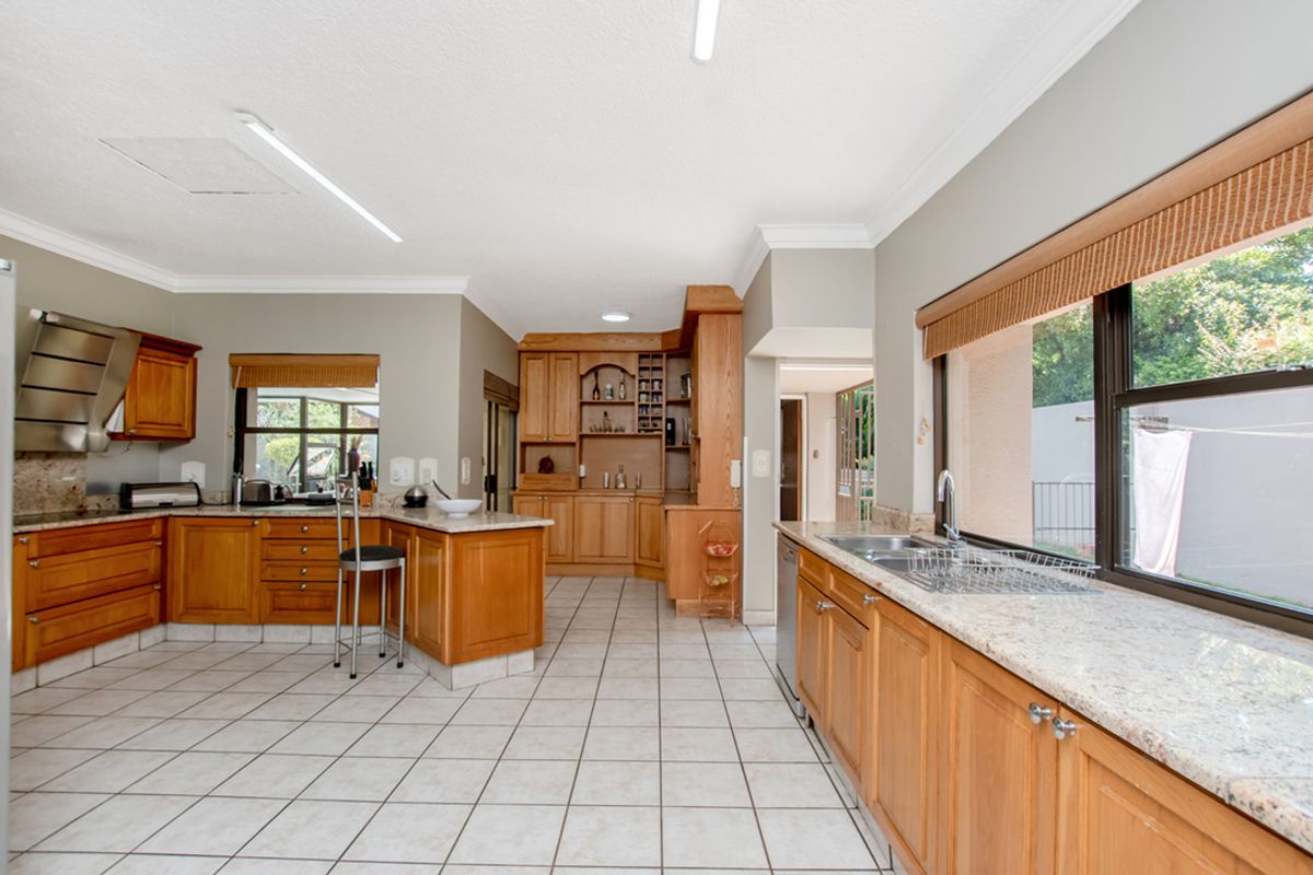 Spacious kitchen featuring extensive wooden cabinetry, granite countertops, double sink, and integrated extractor fan with tiled flooring throughout.