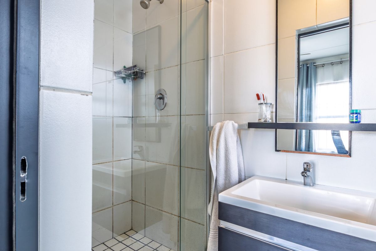 Compact bathroom featuring a glass-enclosed shower with tiled walls and a modern vanity unit with an integrated basin and mirror.