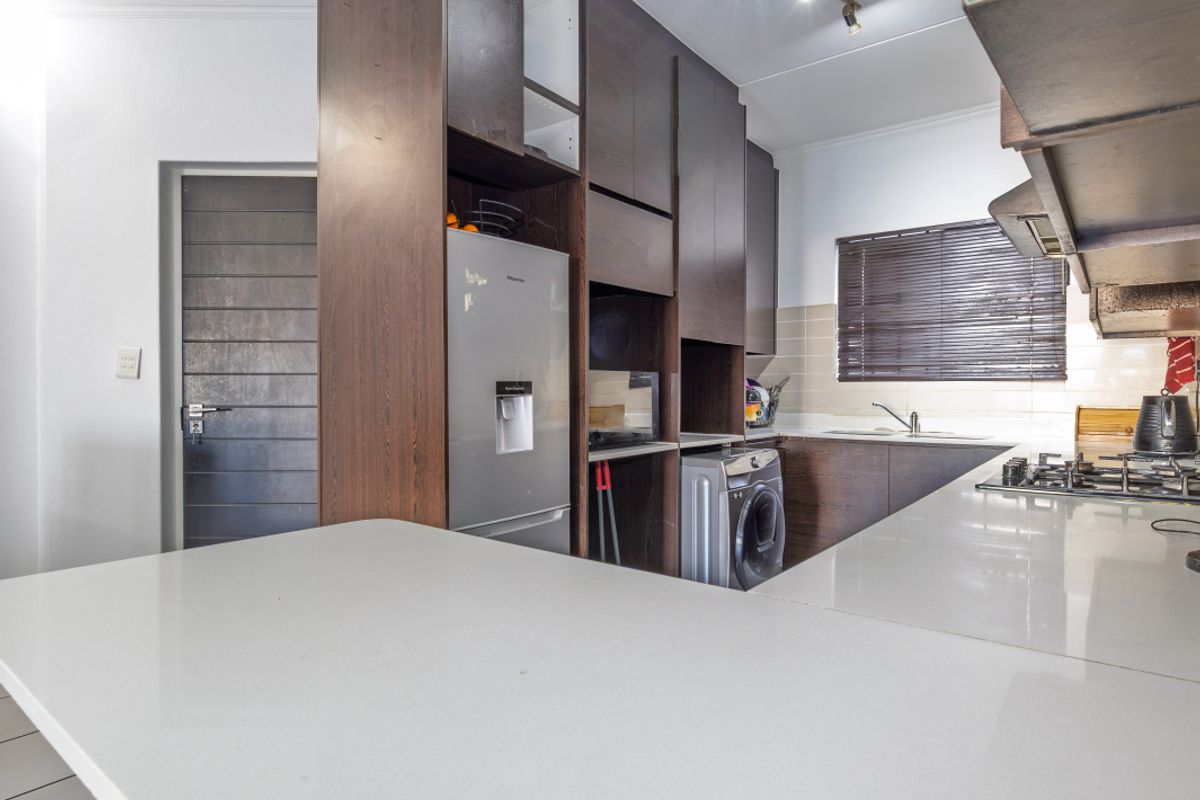 Modern kitchen featuring dark wood cabinetry, stone countertops, integrated appliance spaces, and a gas hob, offering a functional and stylish cooking area.
