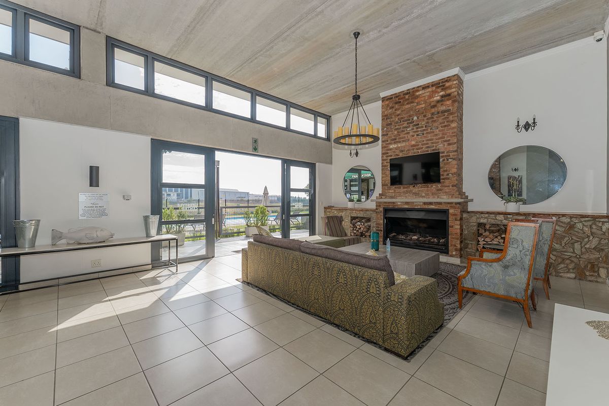 Spacious living area featuring a prominent brick fireplace, exposed concrete ceiling, large windows, and direct access to an outdoor patio area.