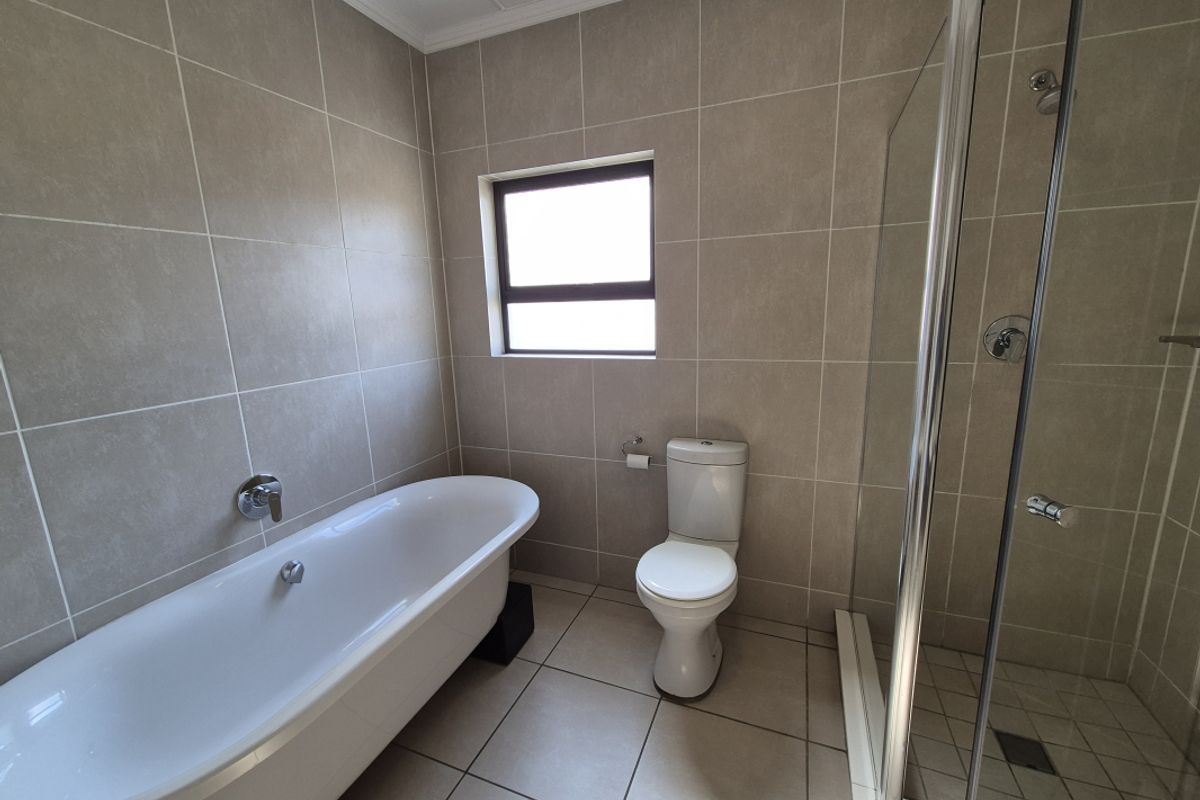 A modern bathroom featuring a freestanding bathtub, a separate glass-enclosed shower, and neutral floor-to-ceiling tiling.