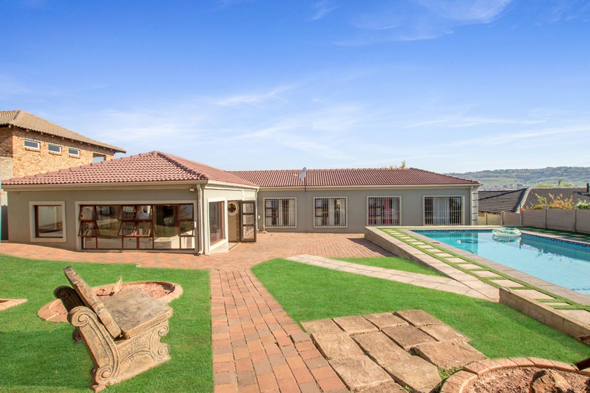 Rear exterior view featuring a paved patio, swimming pool, landscaped lawn, and brick pathways, showcasing the property's outdoor entertainment space.