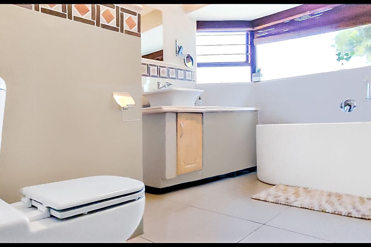 A functional bathroom featuring a white bathtub, a vanity with a vessel sink, a toilet, and a bidet, complemented by large windows.