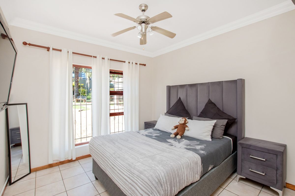 A well-maintained bedroom featuring tiled flooring, a ceiling fan, and direct access to the exterior through a glass door.