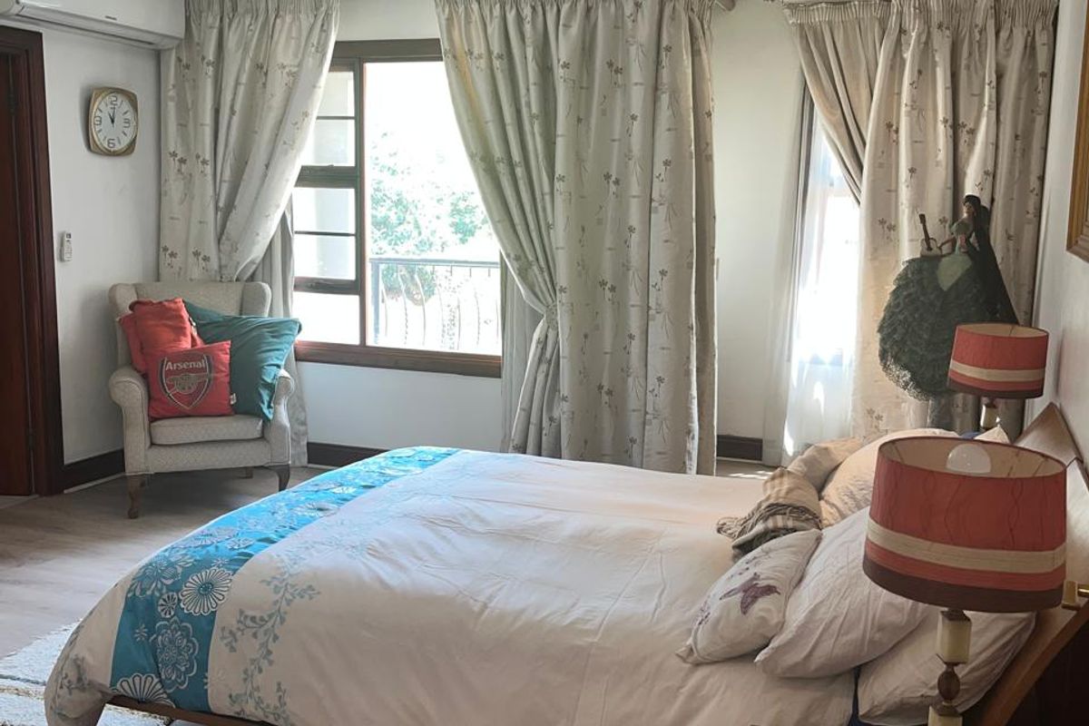 A well-lit bedroom featuring laminate flooring, recessed ceiling lighting, and a wall-mounted air conditioning unit.