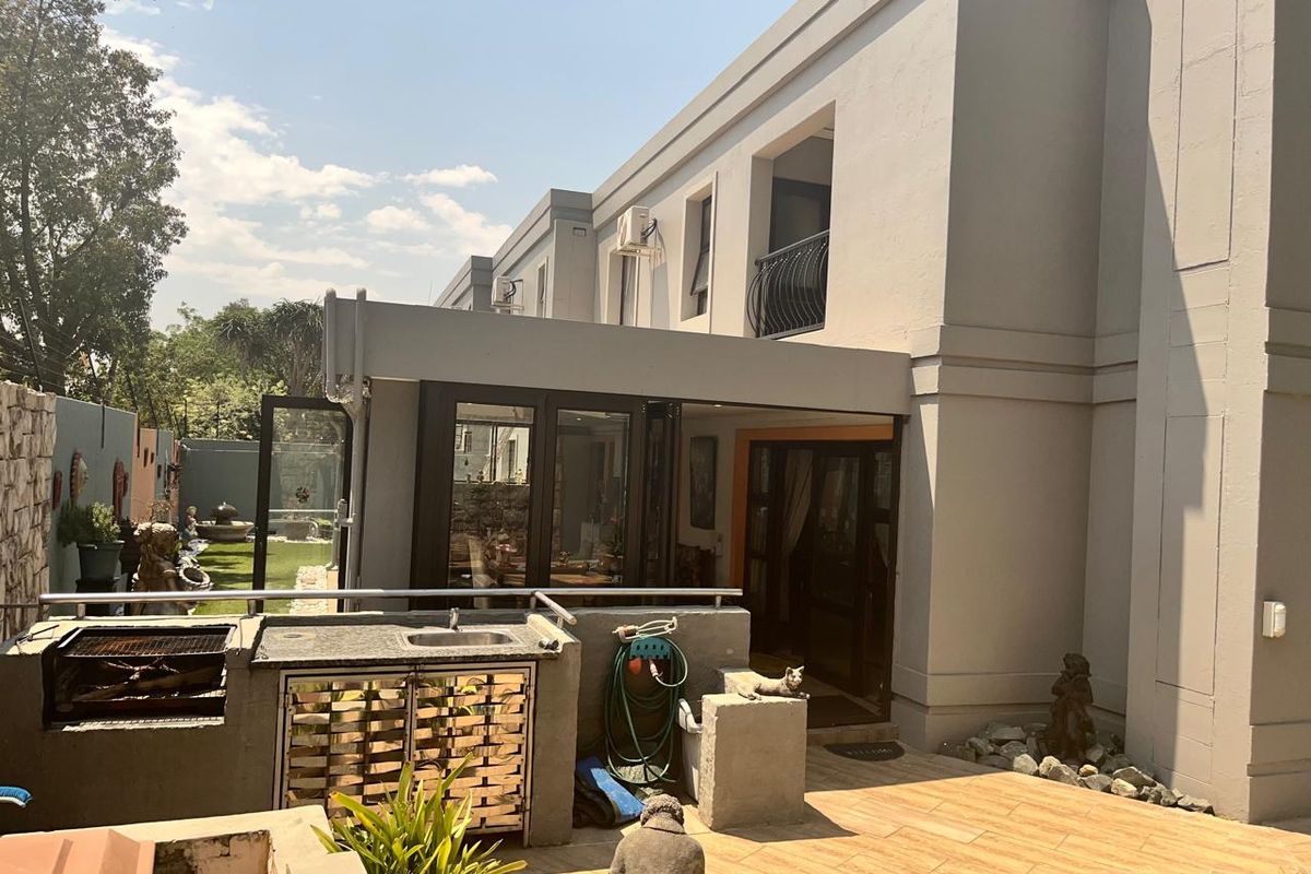 Rear exterior view featuring a paved patio area with a built-in braai, stainless steel cabinetry, sink, and access to the home via folding glass doors.
